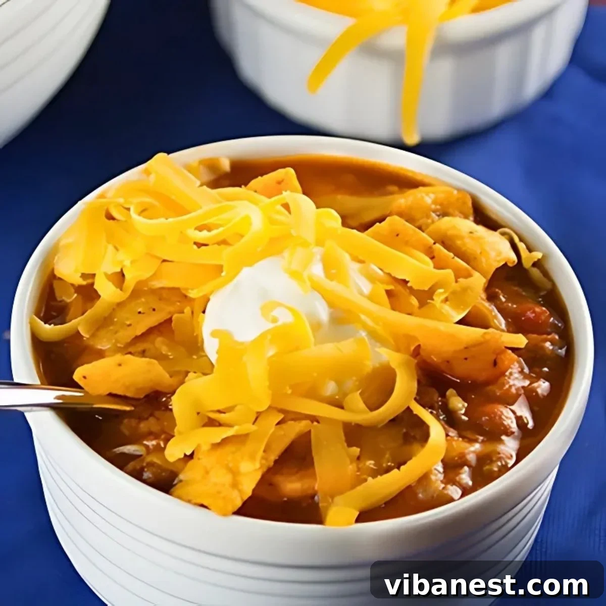 Slow-Simmered Comfort Chili 2 A bowl of slow cooker chili, generously topped with shredded cheese, a dollop of sour cream, and crunchy Fritos, ready to be enjoyed.
