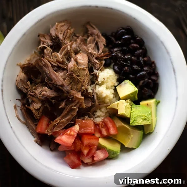 A full, vibrant Slow Cooker Carnitas Burrito Bowl with cauliflower rice and fresh ingredients, ready to eat