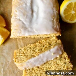 A beautifully moist lemon zucchini bread with a glistening glaze drizzled generously on top, artfully sliced on a rustic cutting board.