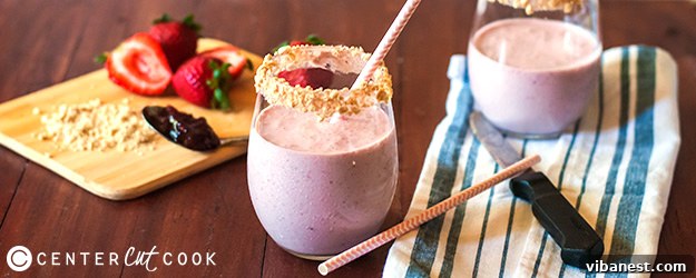 Delicious Strawberry Cheesecake Smoothie in a tall glass, garnished with fresh strawberries and graham cracker crumbs