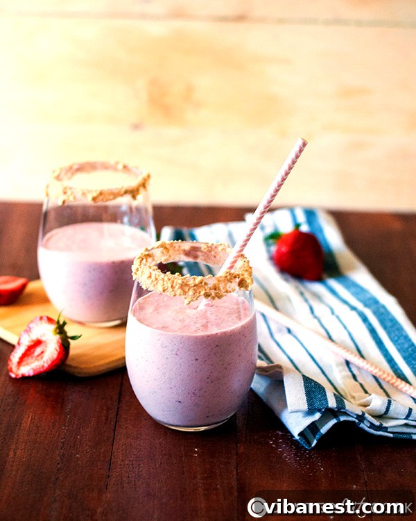 Close-up shot of a creamy strawberry cheesecake smoothie, showing its thick texture and vibrant pink color, garnished with crumbs