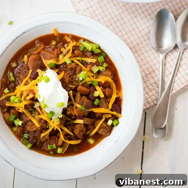A bowl of slow cooker chili with kidney and pinto beans, garnished with Greek yogurt, cheddar cheese, and green onions