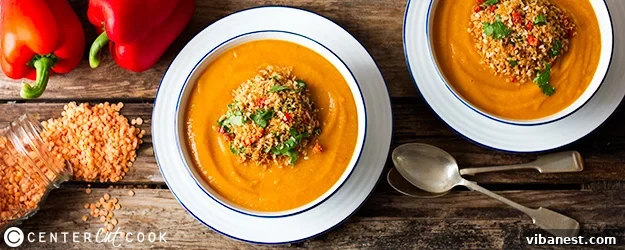 A steaming bowl of vibrant orange lentil vegetable soup, garnished with fresh parsley and a swirl of cream.