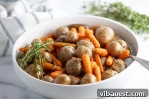 Golden Garlic Roasted Potatoes and Carrots 4 Baby carrots and potatoes in a serving dish on a table alongside a roasted chicken dinner, ready to be served.