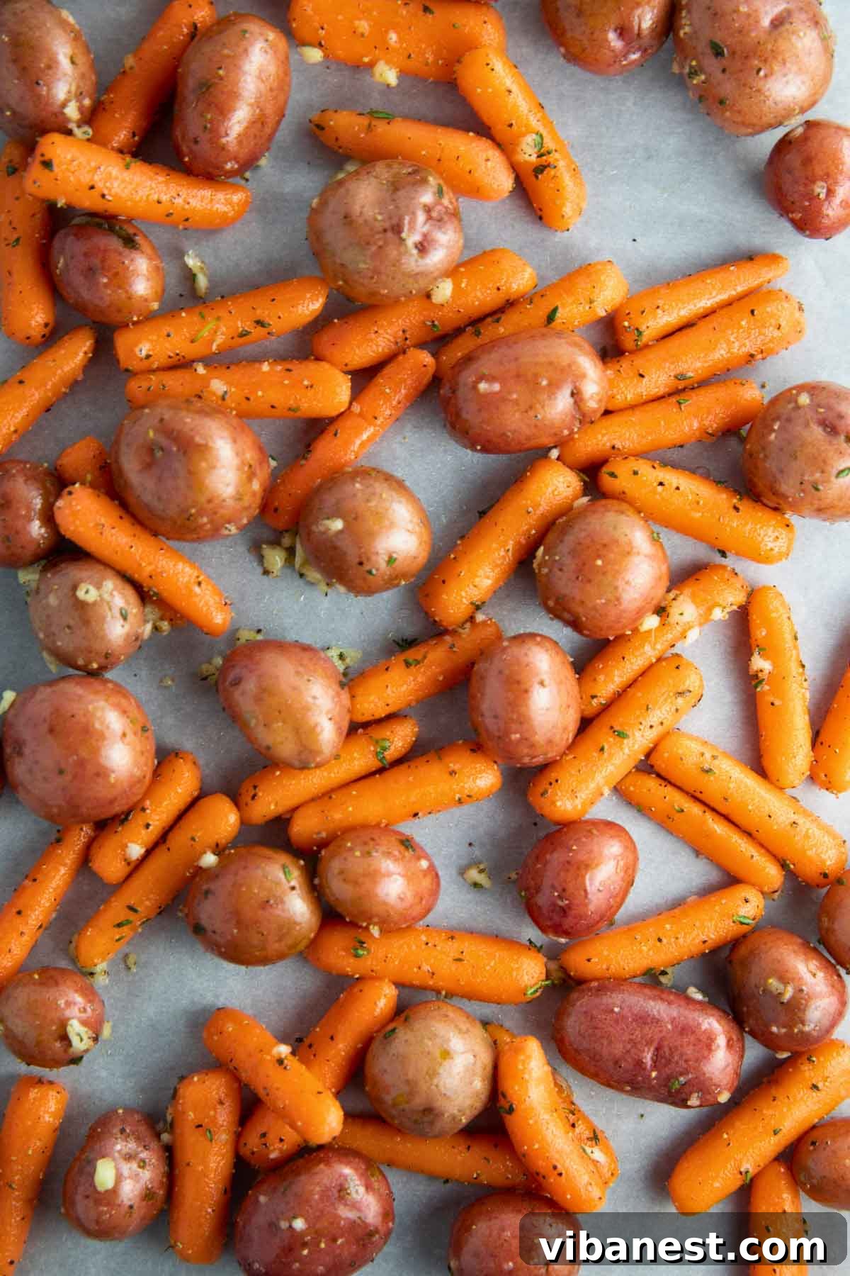 Golden Garlic Roasted Potatoes and Carrots 6 Baby potatoes and carrots tossed with olive oil, garlic, thyme, salt, and pepper, evenly spread on a sheet pan lined with parchment paper, ready to roast in the oven.