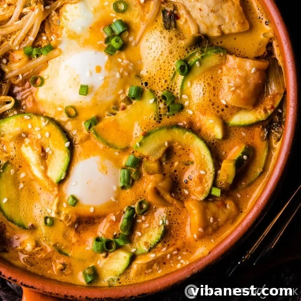 A close-up of a pot of Korean Tofu Stew ready to be served, garnished with fresh green onions and a drizzle of sesame oil.