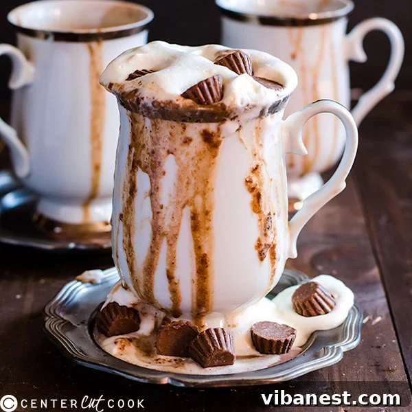 Mugs of slow cooker peanut butter hot chocolate topped with whipped cream and mini chocolate peanut butter cups