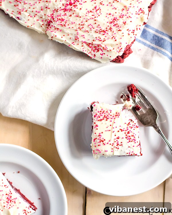 Close-up of a stack of red velvet sugar cookie bars with thick cream cheese frosting and sprinkles.