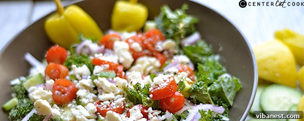 Freshly prepared chopped kale Greek salad in a large serving bowl, garnished with lemon pepper.