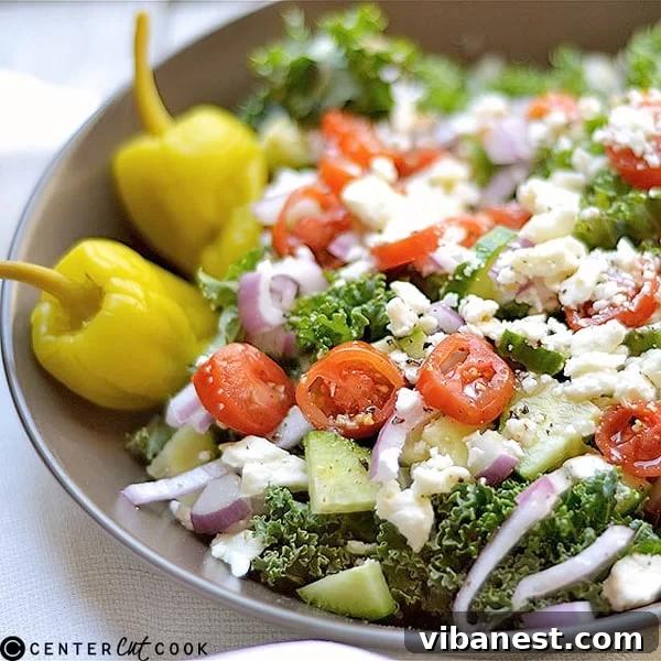 A bowl of Chopped Kale Greek Salad with dressing, ready to be served.