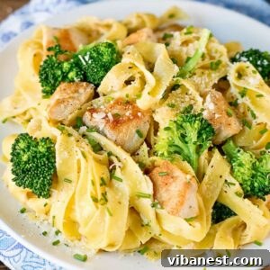 Close-up of fettuccine Alfredo with chicken and broccoli on a plate, garnished with fresh herbs.
