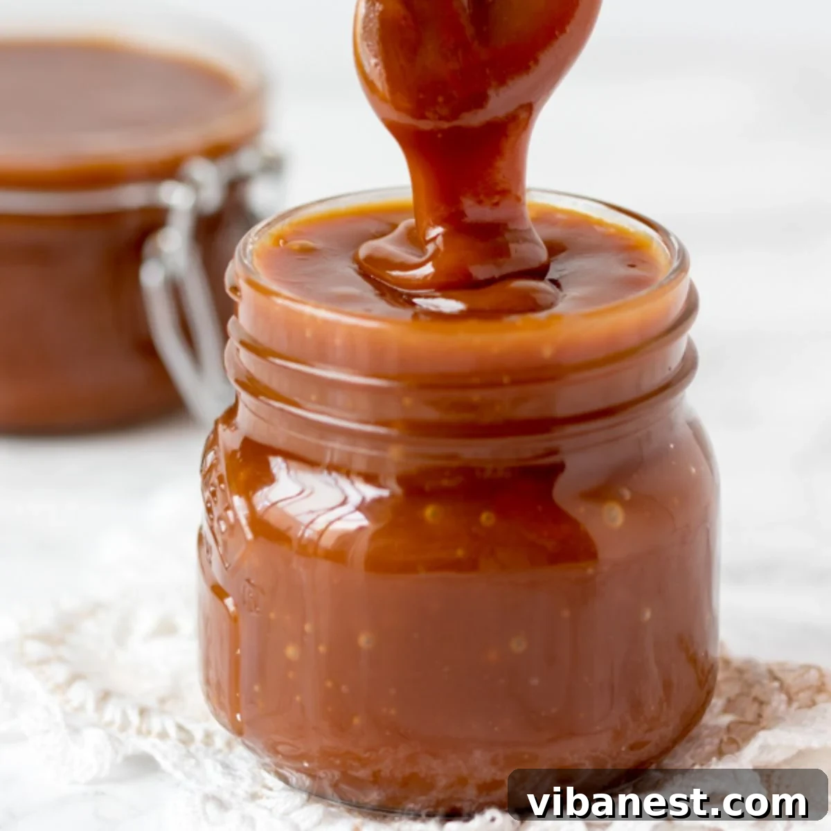 Homemade Caramel Perfection 2 Jar of glistening homemade caramel sauce with a spoon dripping caramel, showcasing its smooth texture