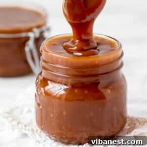 Jar of homemade caramel sauce with a spoon pulling out a string of caramel
