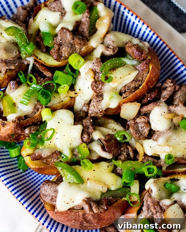 Cheesesteak Potato Skins with Gouda Cheesesteak filling in potato skins, topped with slices of gouda cheese, ready for the oven