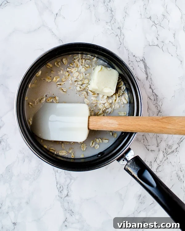 how-to-make-oats-stovetop A small saucepan with oats, milk, and butter simmering on the stove, beginning to thicken.
