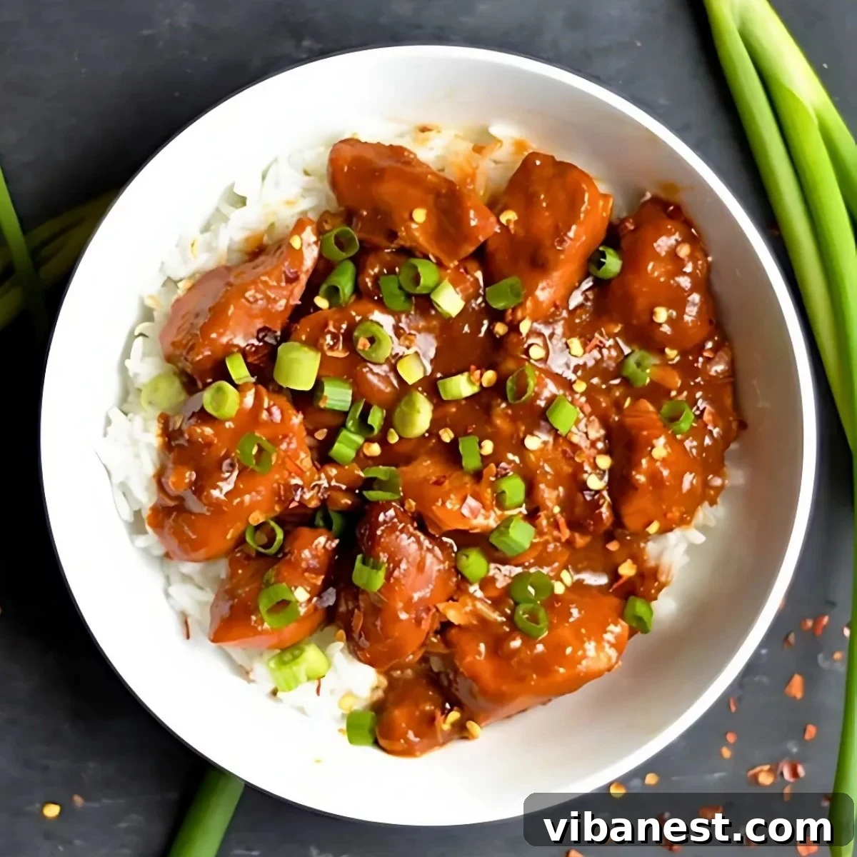 Easy Slow Cooker General Tso Chicken 2 bowl of slow cooker general Tso's chicken served over white rice and garnished with green onions.