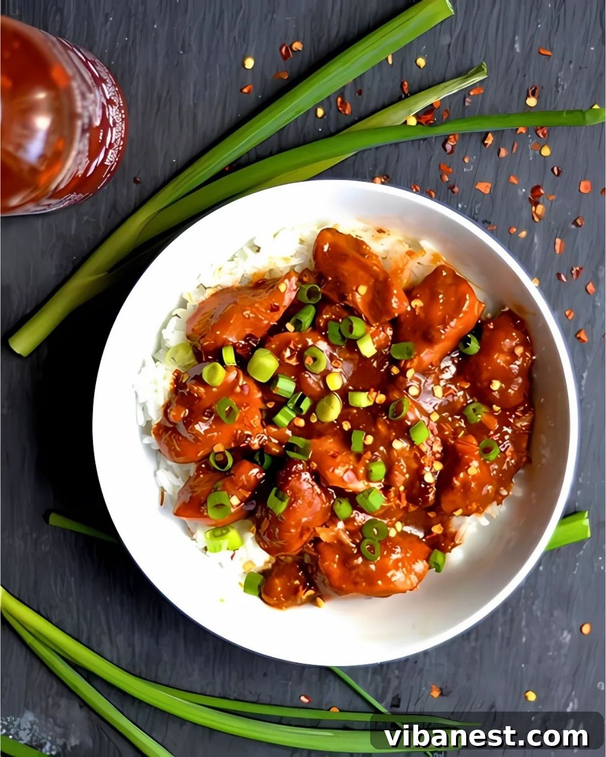 Easy Slow Cooker General Tso Chicken 4 overhead photo of a bowl of general tso's chicken made in the slow cooker served with white rice and garnished with chopped green onions and red pepper flake.