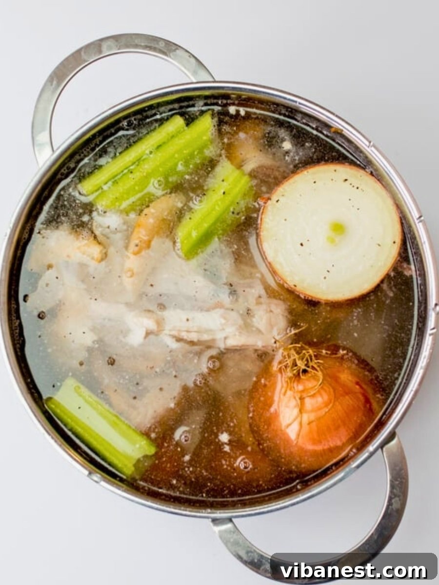 Mastering Homemade Chicken Stock 6 Chicken stock simmering gently on the stove with vegetables and herbs visible.