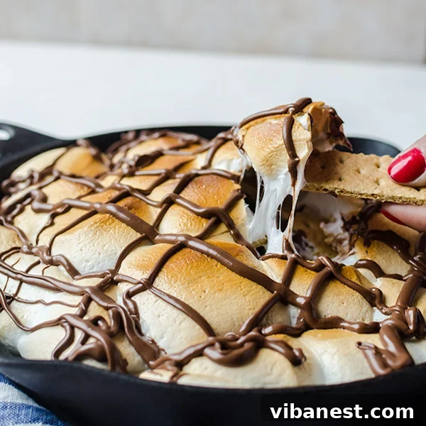 A close-up shot of the finished S'mores Nachos in a cast iron skillet, with a fork digging into the gooey layers