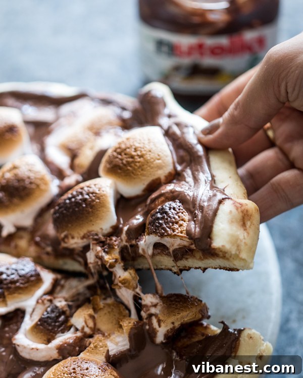S'mores Chocolate Pizza - Ready to Enjoy A freshly baked S'mores Chocolate Pizza on a wooden cutting board, sliced and ready to serve