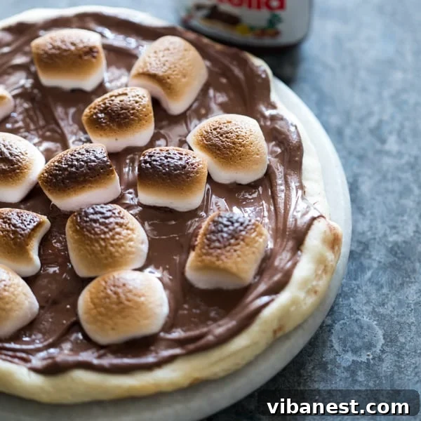S'mores Chocolate Pizza served on a rustic wooden board, with a slice removed showing the gooey interior