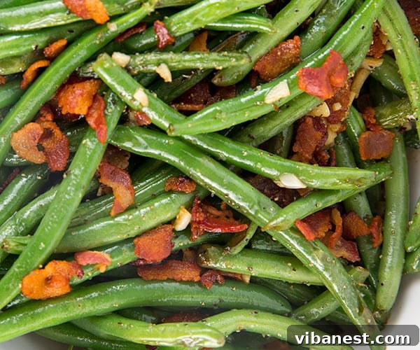 how-to-make-green-beans-3.jpg Close-up of green beans sautéing in a skillet with crispy bacon