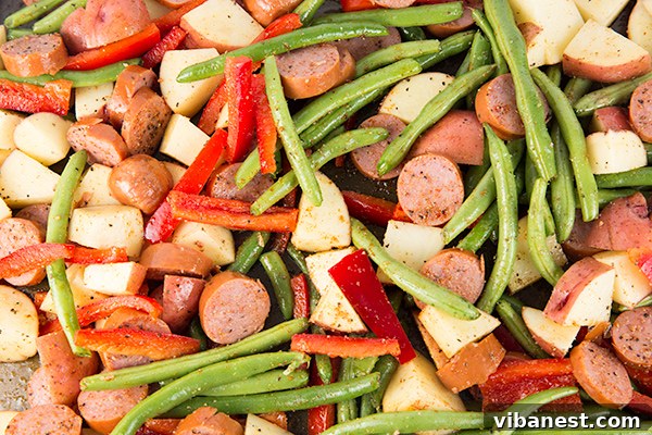 one-pan-sausage-potatoes-3.jpg Chopped sausage and vegetables mixed on a baking sheet before roasting