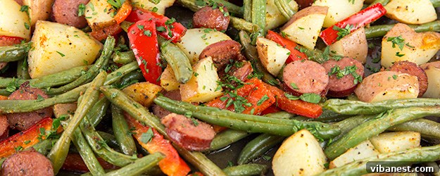 one-pan-sausage-potatoes-1.jpg A full sheet pan of roasted sausage, potatoes, and vegetables, ready to serve