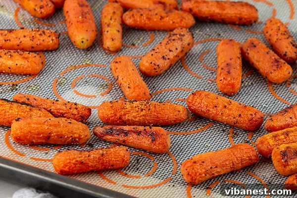 oven-roasted-baby-carrots-2.jpg A serving of oven-roasted baby carrots, garnished with fresh herbs, on a white plate.