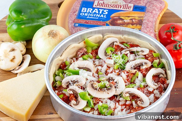Deep-dish pizza assembled with sauce and toppings over brat sausage