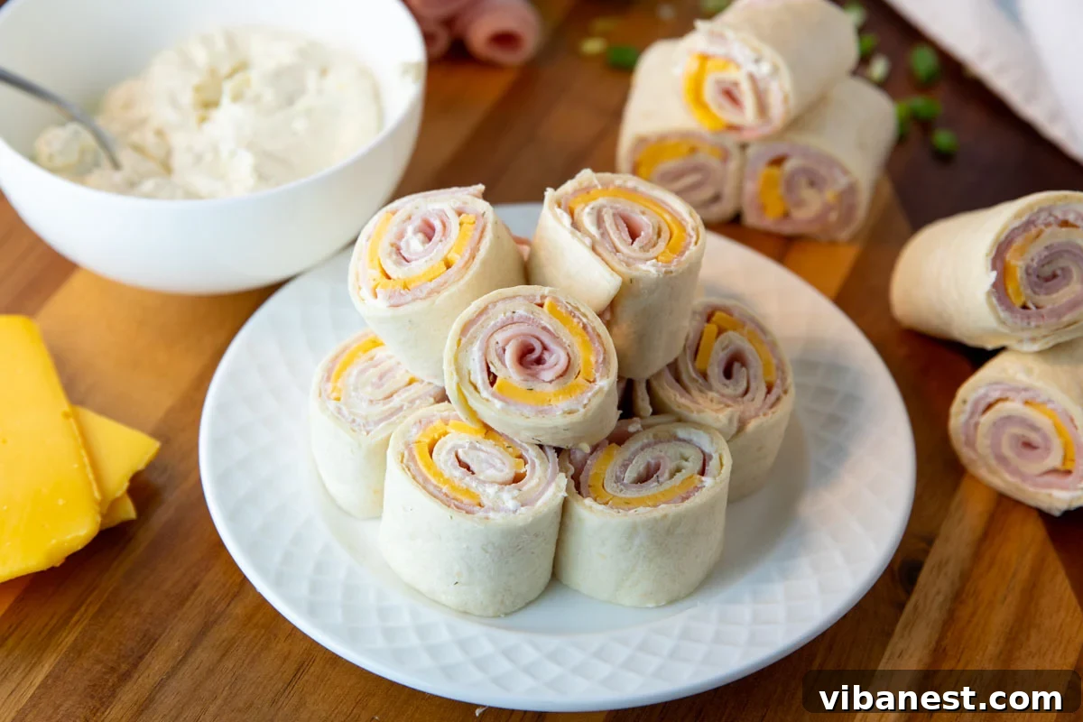 Savory Ham and Cheese Swirls 5 ham and cheese pinwheels on a plate with bowl of seasoned cream cheese, ham and cheese pinwheels, and slices of cheese surrounding.