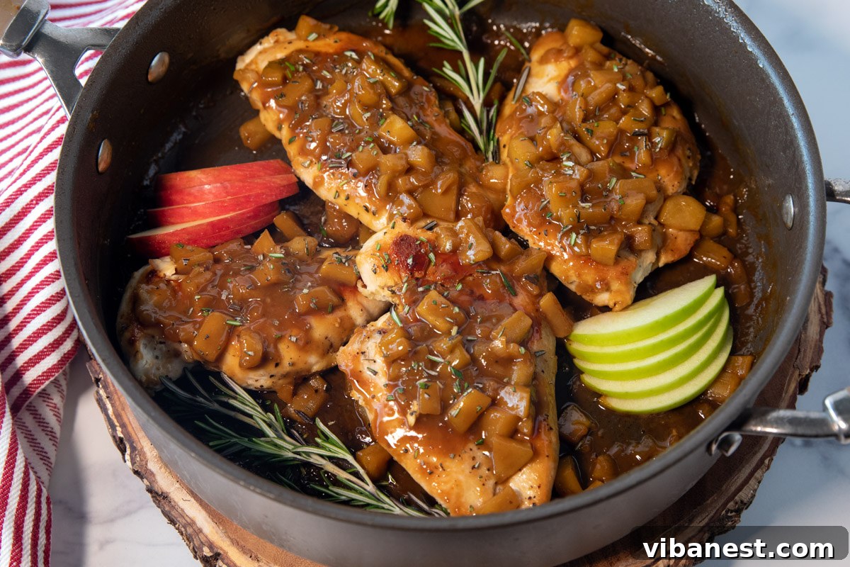 Harvest Skillet Chicken with Apple Cider Glaze 2 A golden-brown pan-seared chicken breast generously coated in a rich, glossy apple cider sauce, adorned with tender diced apples and fresh rosemary, presented in a rustic cast-iron skillet, perfect for a cozy fall meal.