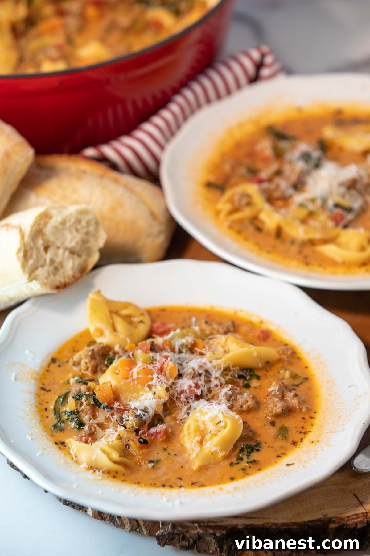 Fiery Italian Sausage Tortellini Soup 2 Two bowls of creamy spicy tortellini soup with slices of crusty bread and spoons on the side.