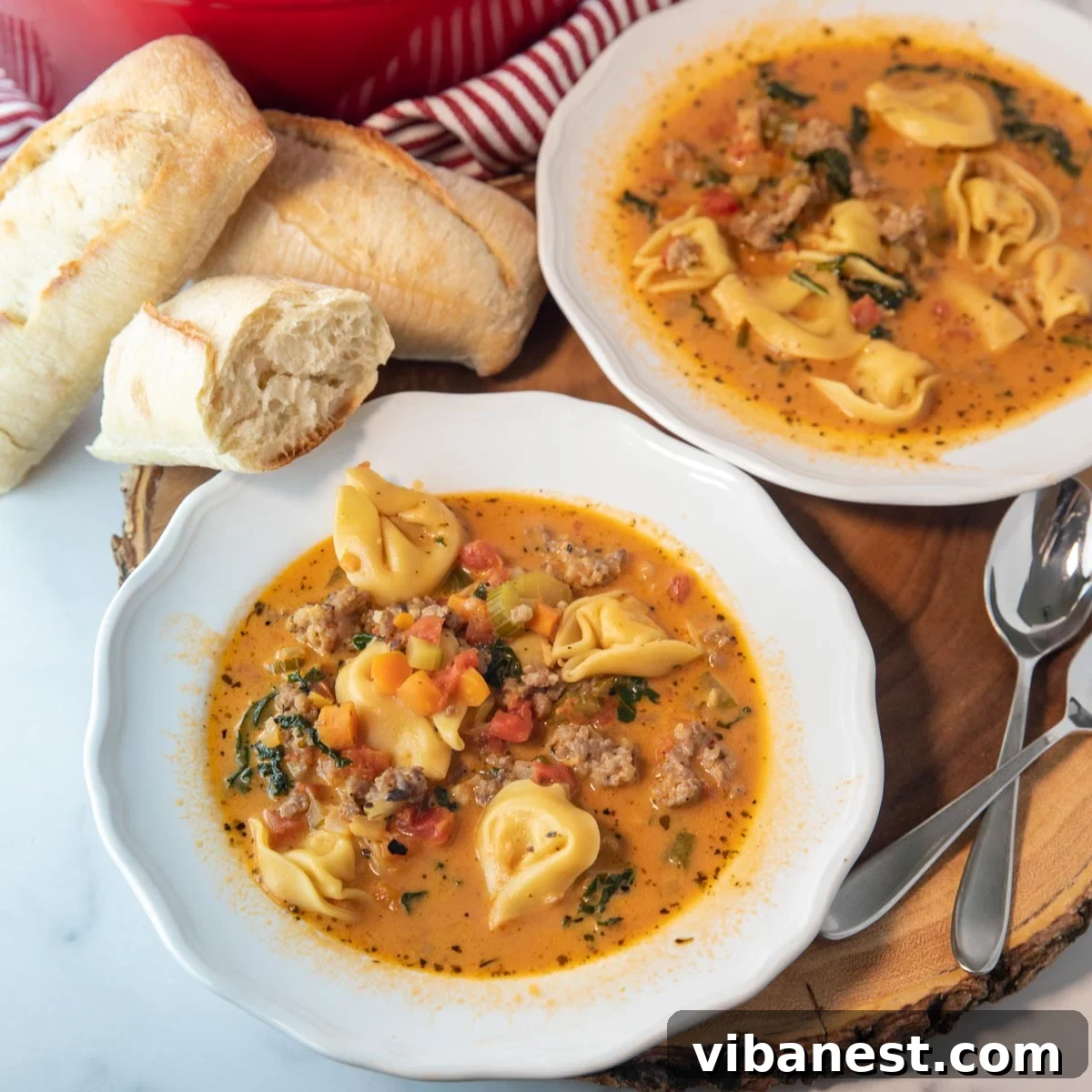 Fiery Italian Sausage Tortellini Soup 5 Two bowls of spicy tortellini soup with bread and spoons sitting beside them on a wooden table.