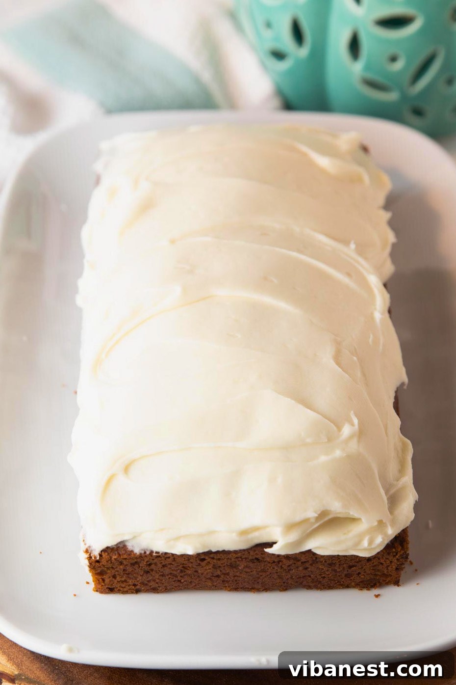 Decadent Pumpkin Bread with Creamy Cheesecake Topping 3 A whole loaf of pumpkin bread with a thick layer of cream cheese frosting on a plate, ready for slicing.