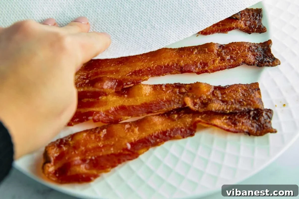 Crispy Oven Bacon Every Time 4 Freshly baked bacon being transferred to a plate lined with paper towels to drain excess grease.