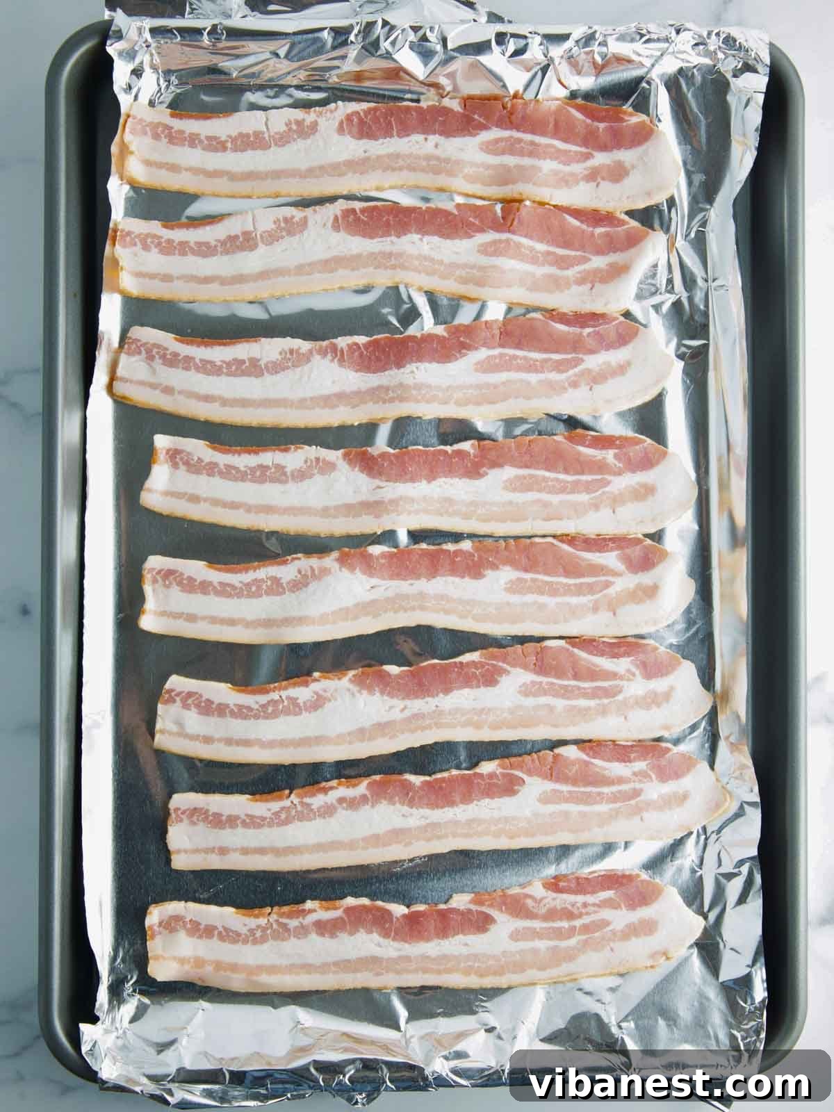 Crispy Oven Bacon Every Time 5 Raw bacon strips evenly spaced on a parchment-lined baking sheet, ready for the oven.