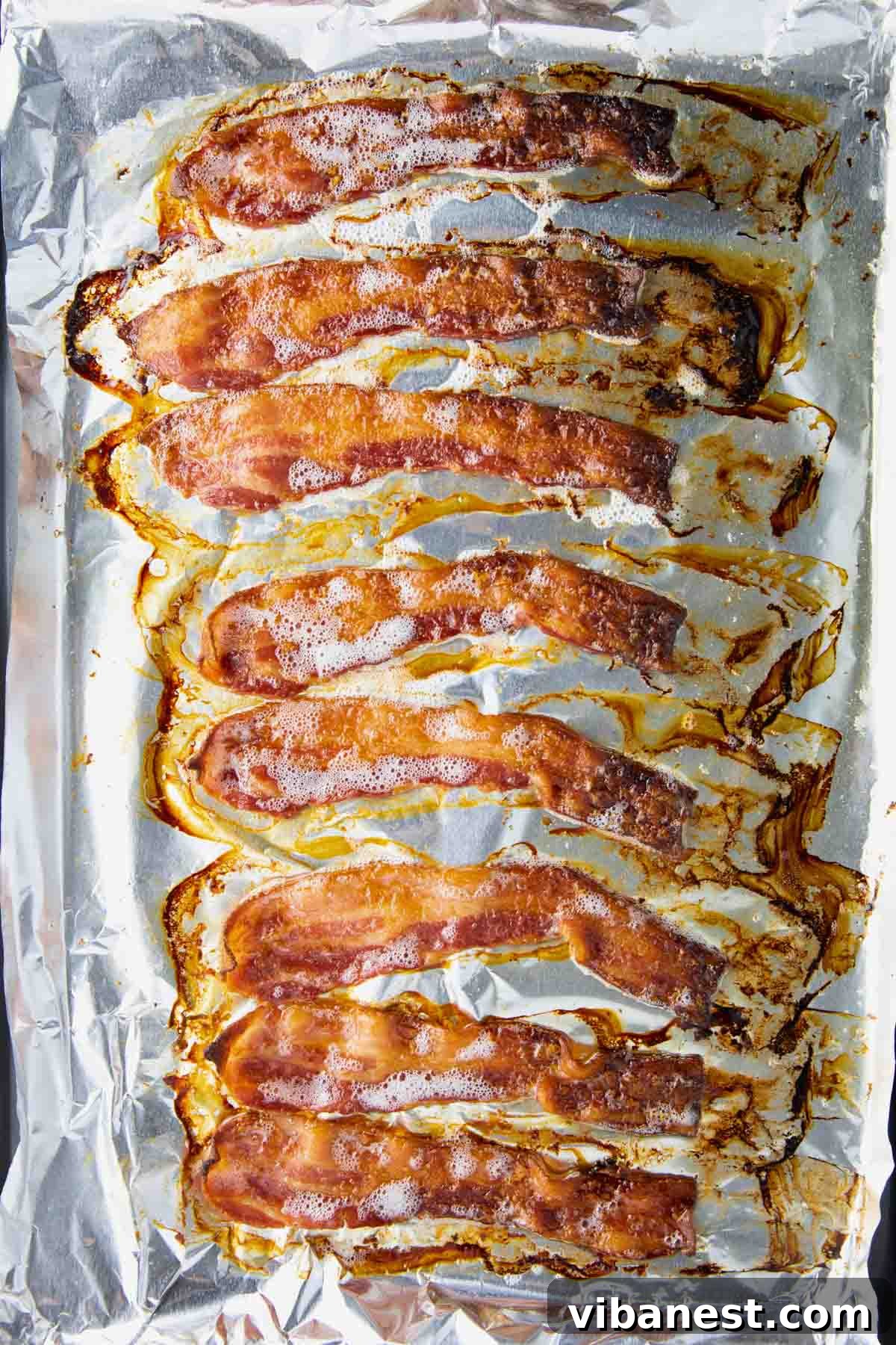 Crispy Oven Bacon Every Time 6 Close-up of bacon cooking and crisping up in the oven on a baking sheet.