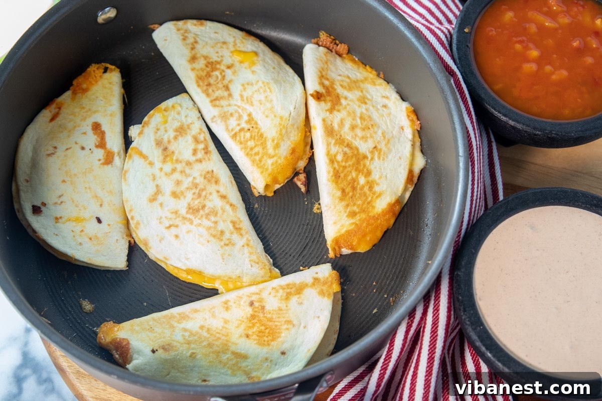 Whip Up Perfect Stovetop Quesadillas 4 Freshly cooked quesadillas sizzling in a frying pan, with serving bowls of salsa and queso nearby, ready for a flavorful meal.