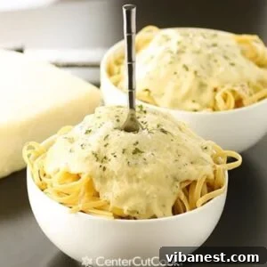A bowl of fettuccine pasta generously coated with creamy Alfredo sauce, garnished with fresh parsley.