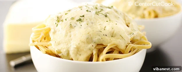 A wide shot of a serving of fettuccine alfredo, with a fork twirled in pasta, highlighting the creamy sauce.