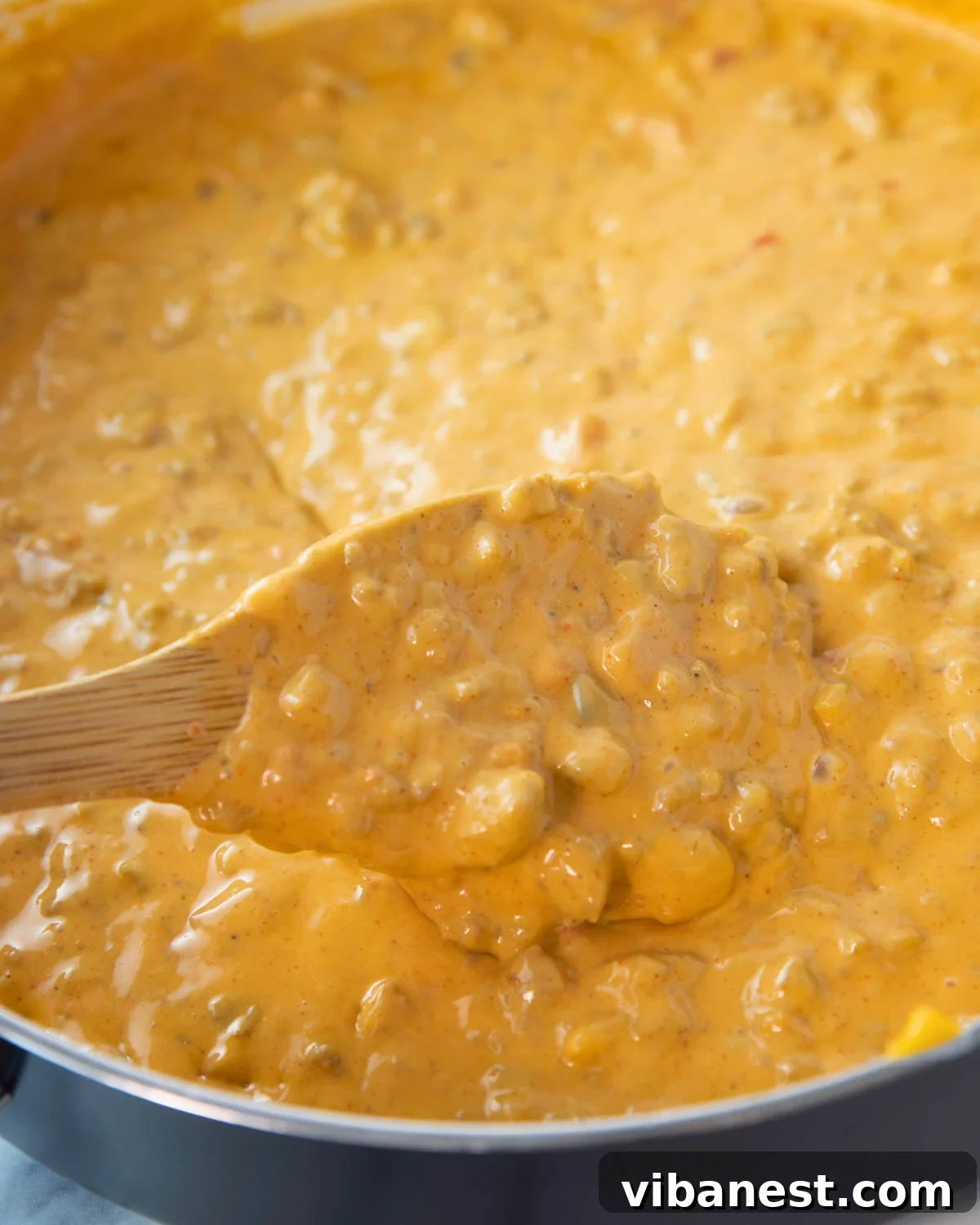 Crowd-Pleasing Rotel Sausage Dip 6 Close-up of a skillet filled with rich, creamy easy Rotel dip with sausage, being stirred with a wooden spoon.