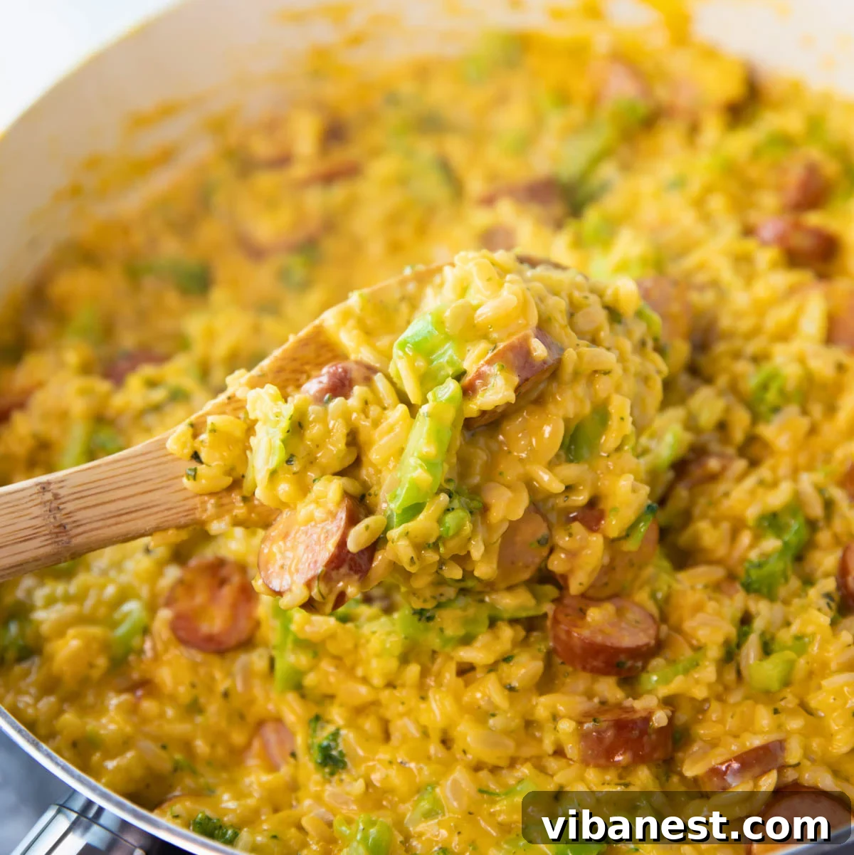 Hearty Cheesy Sausage and Rice Skillet 2 skillet of cheesy sausage and rice skillet with a wooden spoon stirring