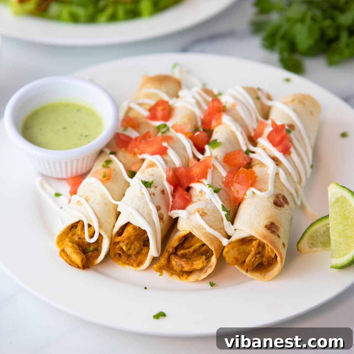 Crispy Air Fryer Chicken Taquitos 6 Two perfectly cooked air fryer chicken taquitos on a white plate, garnished with a dollop of sour cream, fresh lime wedges, and cilantro