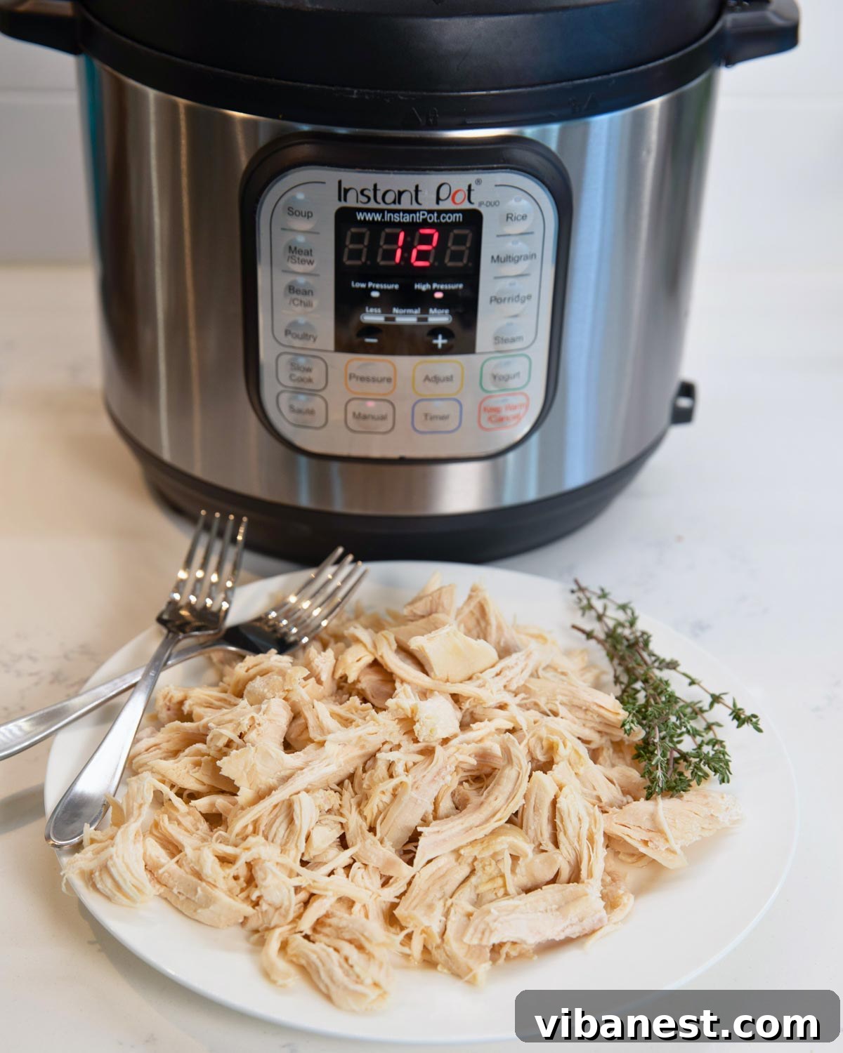 Effortless Instant Pot Pulled Chicken 5 plate of easy instant pot shredded chicken with two forks, instant pot sitting in background.