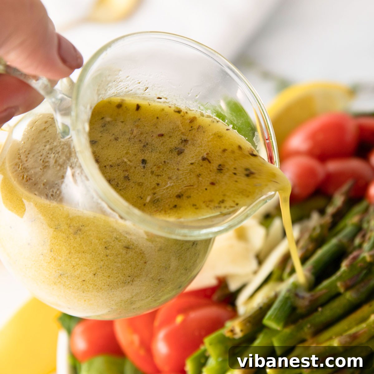 Smoky Grilled Asparagus Salad 8 A woman's hand pouring homemade lemon vinaigrette dressing over a fresh grilled asparagus salad.