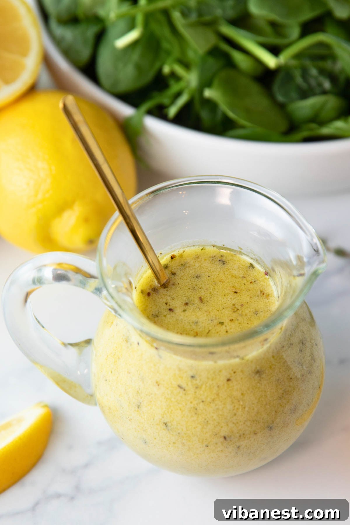 Zesty Lemon Vinaigrette 6 A jar of homemade lemon vinaigrette dressing sits on a rustic wooden surface, with fresh spinach and lemons in the background, ready for a healthy meal.