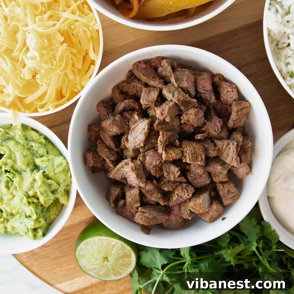 Air Fryer Fajita Burrito Steak 2 Overhead shot of a vibrant bowl of air fryer steak for fajitas, surrounded by an array of colorful fajita and quesadilla toppings.