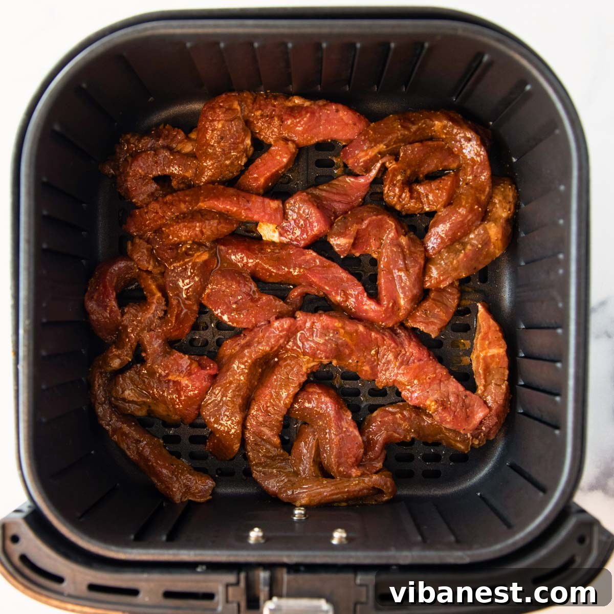 Air Fryer Fajita Burrito Steak 3 Close-up overhead view of marinated steak strips arranged in an air fryer basket, ready for cooking.