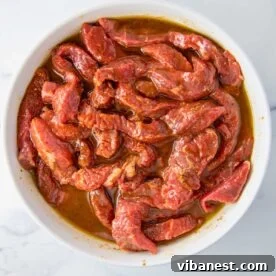 Overhead shot of sirloin steak strips marinating in a flavorful fajita marinade in a bowl.